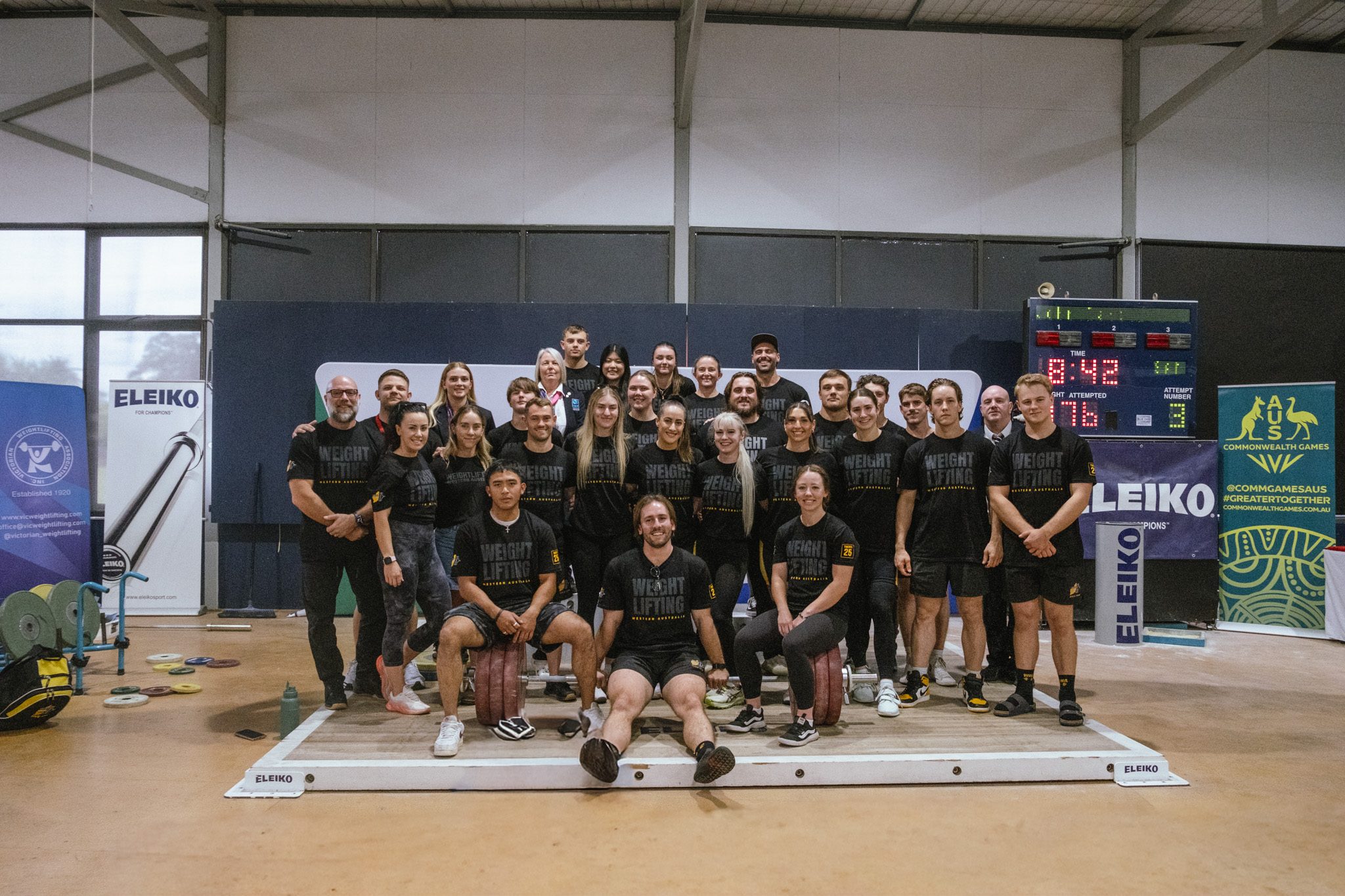 The Weightlifting Western Australia squad on the competition platform, grouped around a loaded barbell
