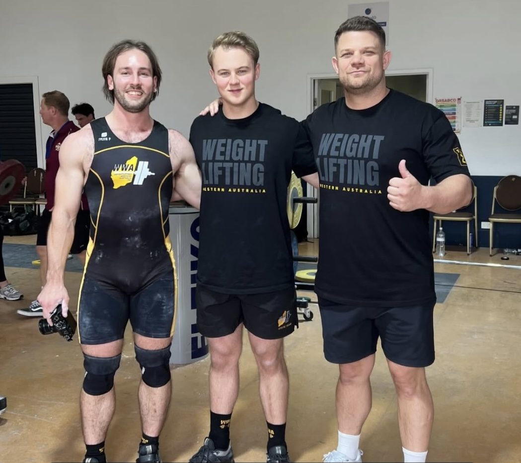 Keanu in a Weightlifting Western Australia singlet, chalked up, with two teammates after lifting